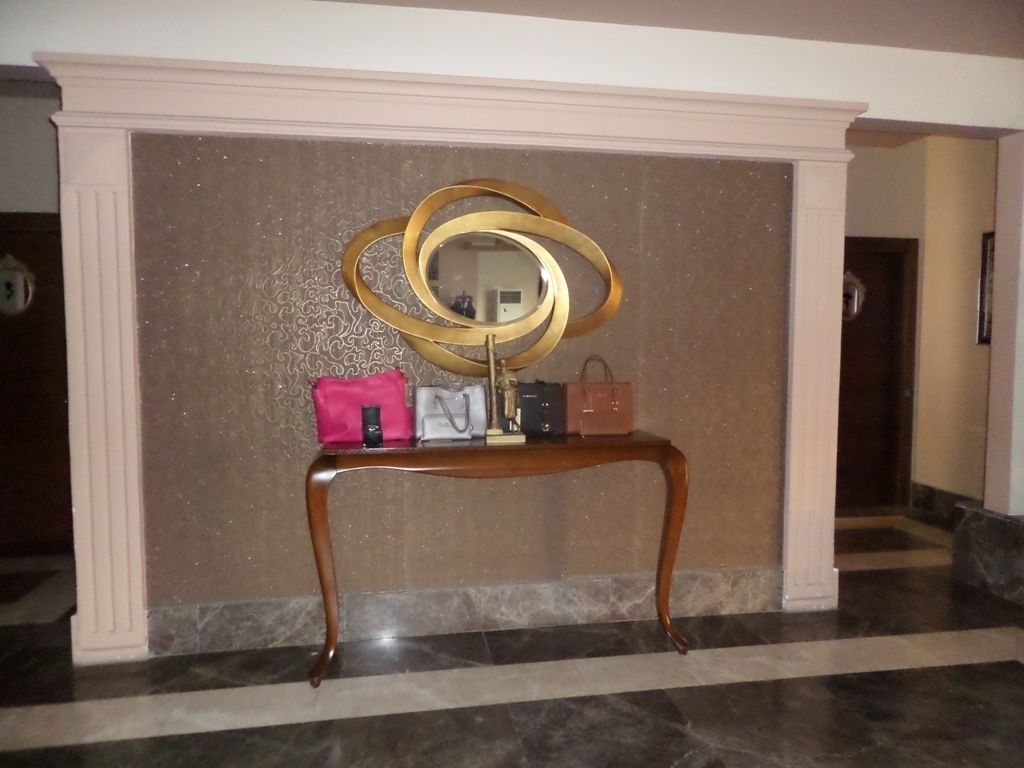 Um hall de entrada com piso de mármore, um console de madeira com bolsas e um espelho decorativo.