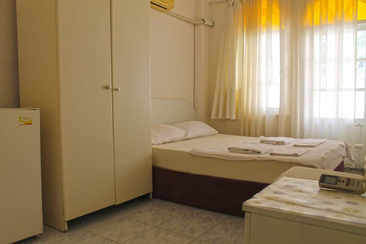 A bedroom with a bed, a bedside table, a wardrobe, and a window with curtains.