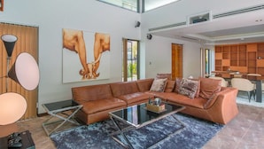Un salon moderne avec un canapé d’angle, une table basse et un grand tableau abstrait accroché au mur.