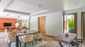 Un salon moderne comprenant un coin repas, un téléviseur à écran plat et une grande fenêtre donnant sur un paysage verdoyant.