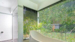 Une salle de bain moderne avec une baignoire sur pieds, une douche en verre et une vue sur un jardin luxuriant, visible à travers une grande fenêtre.