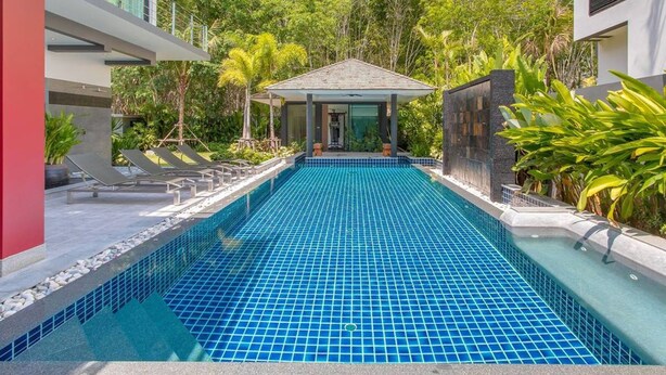 Un espace piscine moderne avec un sol carrelé, entouré d’une végétation luxuriante et doté d’un coin salon abrité.