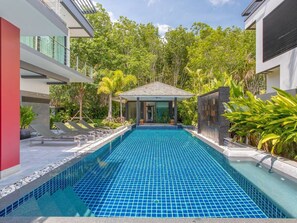 A modern pool area with a tiled floor, surrounded by lush greenery and a covered seating area.