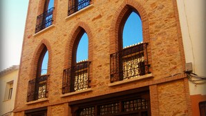 Un bâtiment historique doté de nombreuses fenêtres en arc de cercle et de balcons, caractérisé par une façade traditionnelle en briques et des portes en bois.