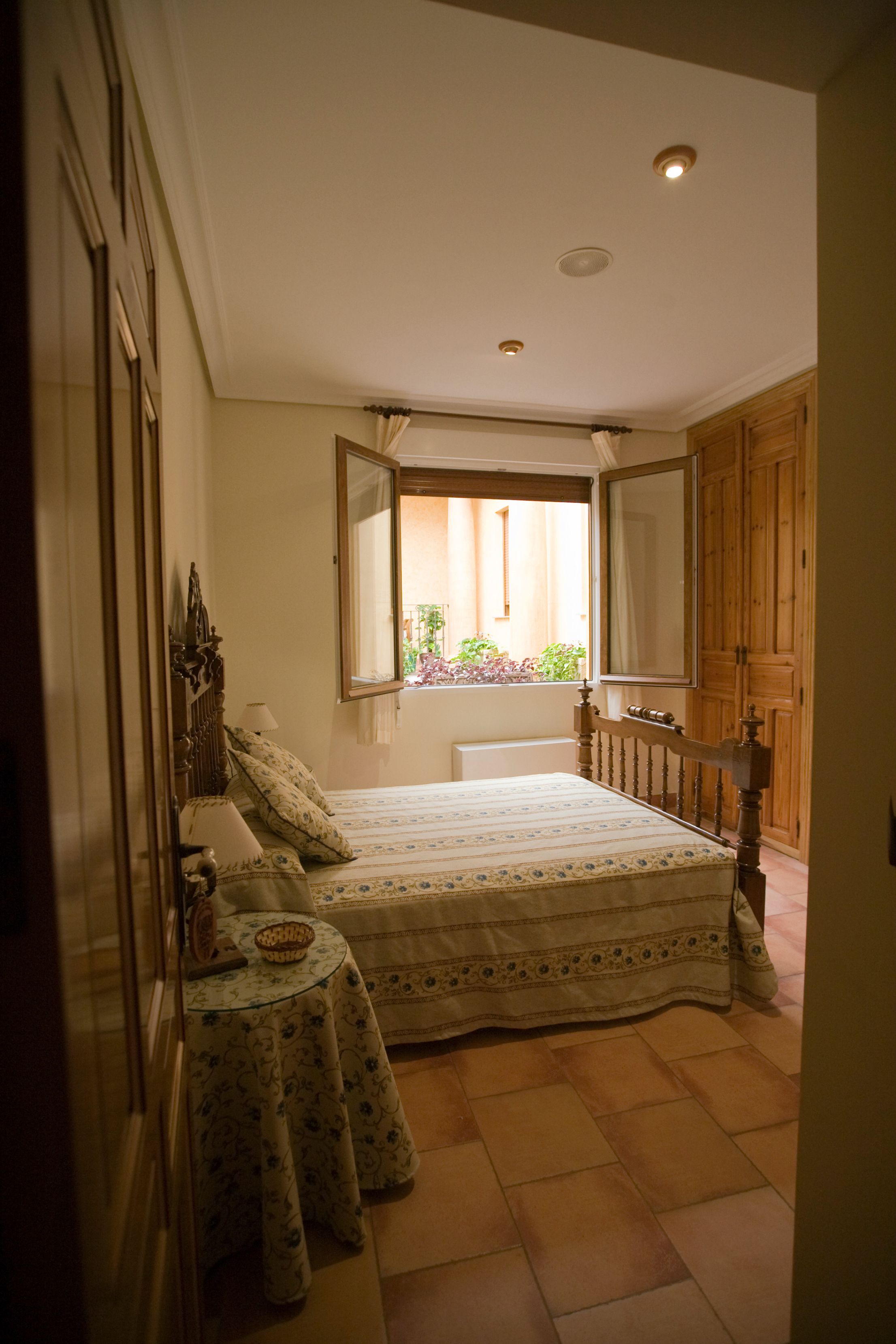 Un dormitorio con cama, mesita de noche, una pequeña mesa redonda y ventana con vistas al exterior.