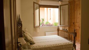 Un dormitorio con cama, mesita de noche, una pequeña mesa redonda y ventana con vistas al exterior.