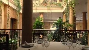 Un espace repas avec une table dressée pour quatre personnes, entouré de verdure et de colonnes.