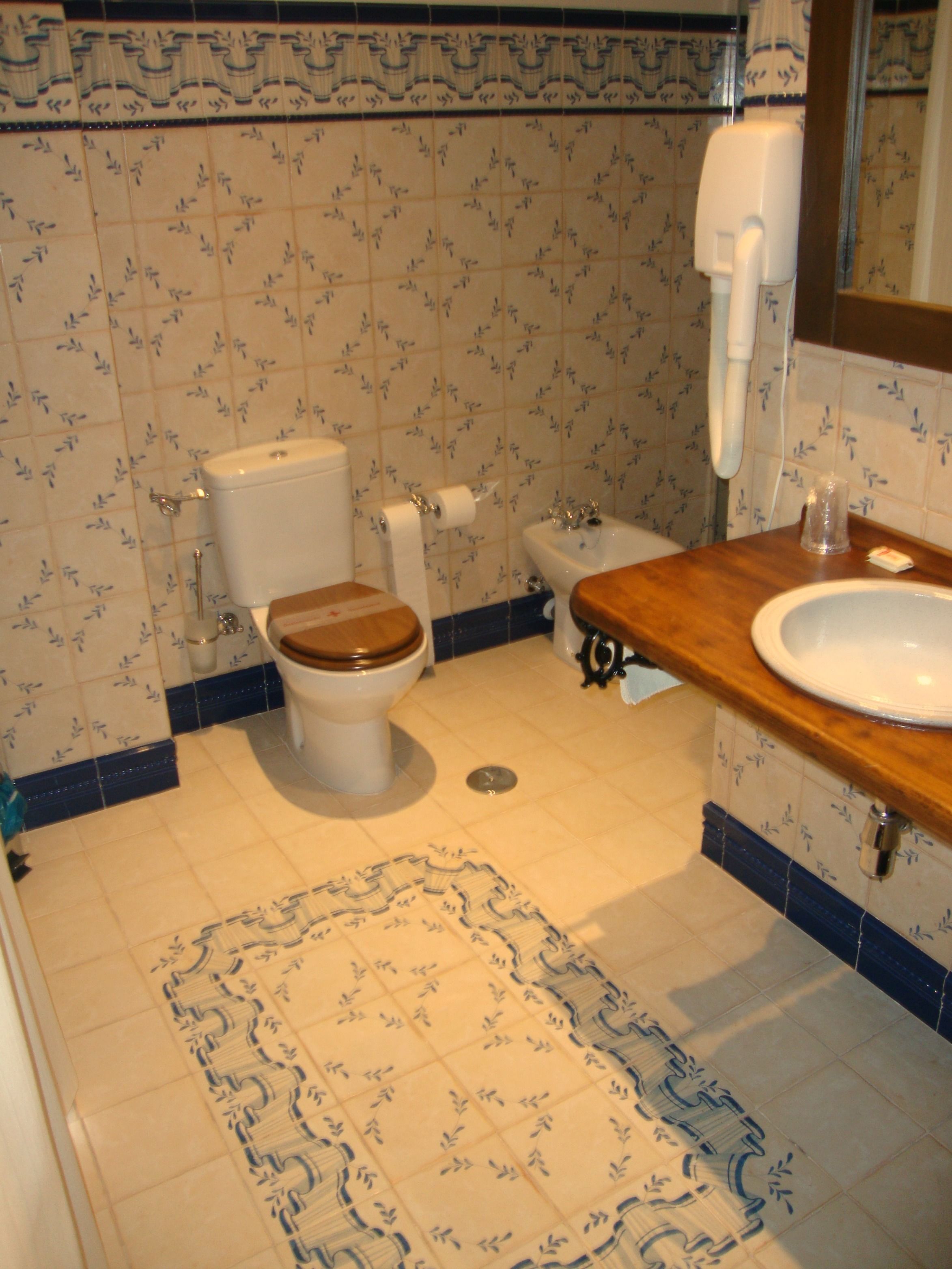 Un baño con inodoro, bidé, lavabo y suelo estampado.