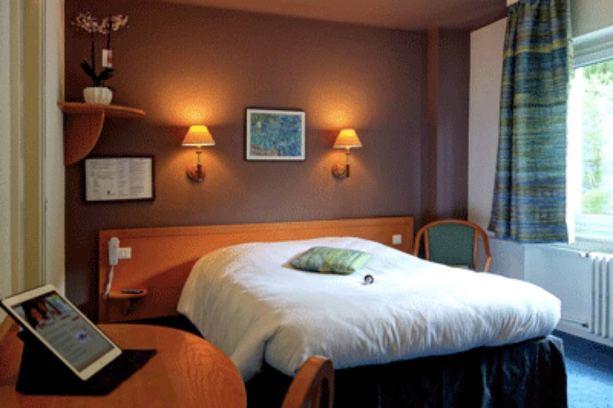 Une chambre d’hôtel avec un lit, deux lampes fixées au mur, une chaise, une petite table et une fenêtre avec des rideaux.