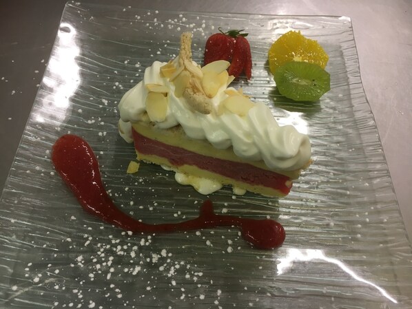 Un postre en un plato de vidrio transparente, con crema batida, fruta y salsa roja.