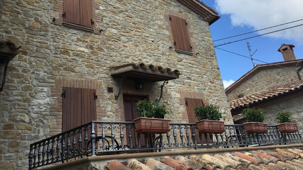 Un bâtiment en pierre avec des volets en bois, un balcon orné de balustrades en fer forgé et des plantes en pot.