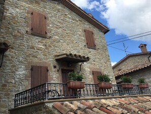 A stone building with wooden shutters, a balcony with wrought iron railings, and potted plants. - Il Poggio (Auditore)