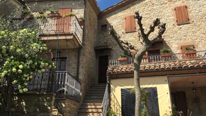 Un bâtiment en pierre doté d’un balcon, d’un escalier et d’un arbre devant.