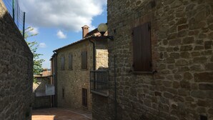 Une étroite ruelle pavée, bordée d’un bâtiment rustique sur la droite, avec une porte en bois et un petit balcon.