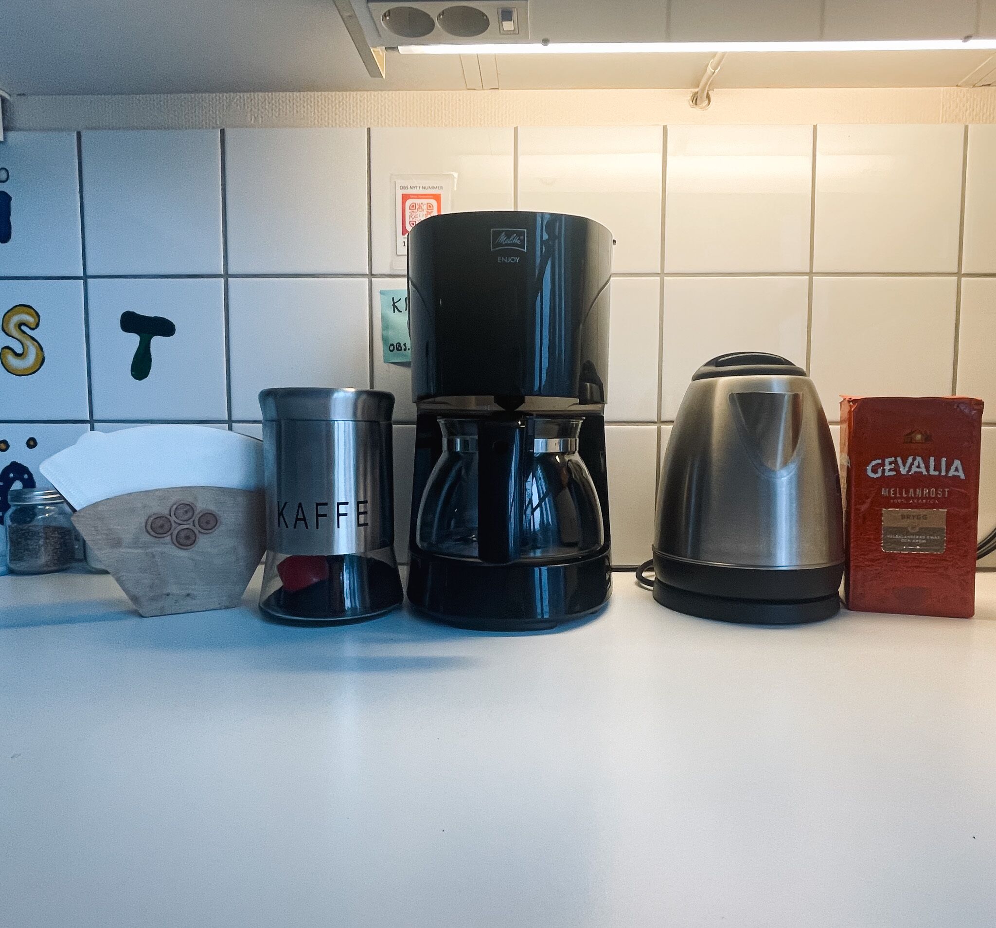 A kitchen counter with a coffee maker, a kettle, and a box of Gevalia coffee.
