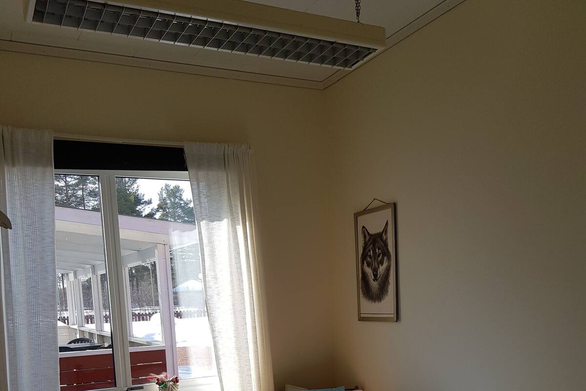Quarto com cama, janela com cortinas, radiador, escrivaninha e quadro na parede.