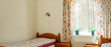 Un dormitorio pequeño y luminoso con una cama de madera, un escritorio pequeño y una ventana con cortinas florales.