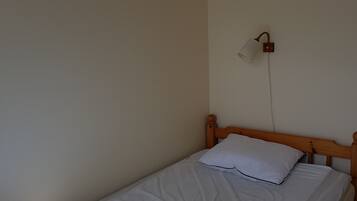 A single bed with a wooden headboard, white bedding, and a white lamp on the wall.