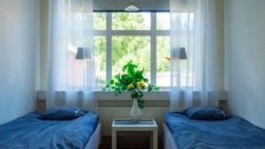Una habitación con dos camas individuales, una mesita con un florero y una ventana con cortinas.