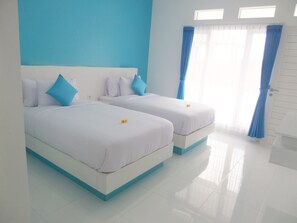 Habitación de hotel con dos camas, ropa de cama blanca, detalles azules y un diseño limpio y luminoso.