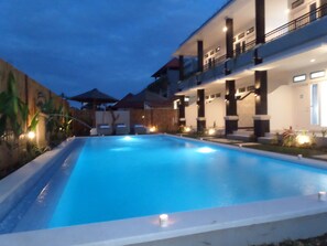 Una piscina con vista a un edificio con varios balcones e iluminación.