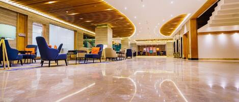 A spacious lobby with a polished marble floor, modern seating arrangements, and a wooden ceiling design.