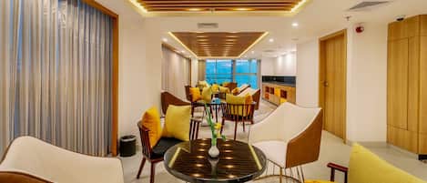 A modern dining area with round tables, yellow and white chairs, and a view of the cityscape through large windows.