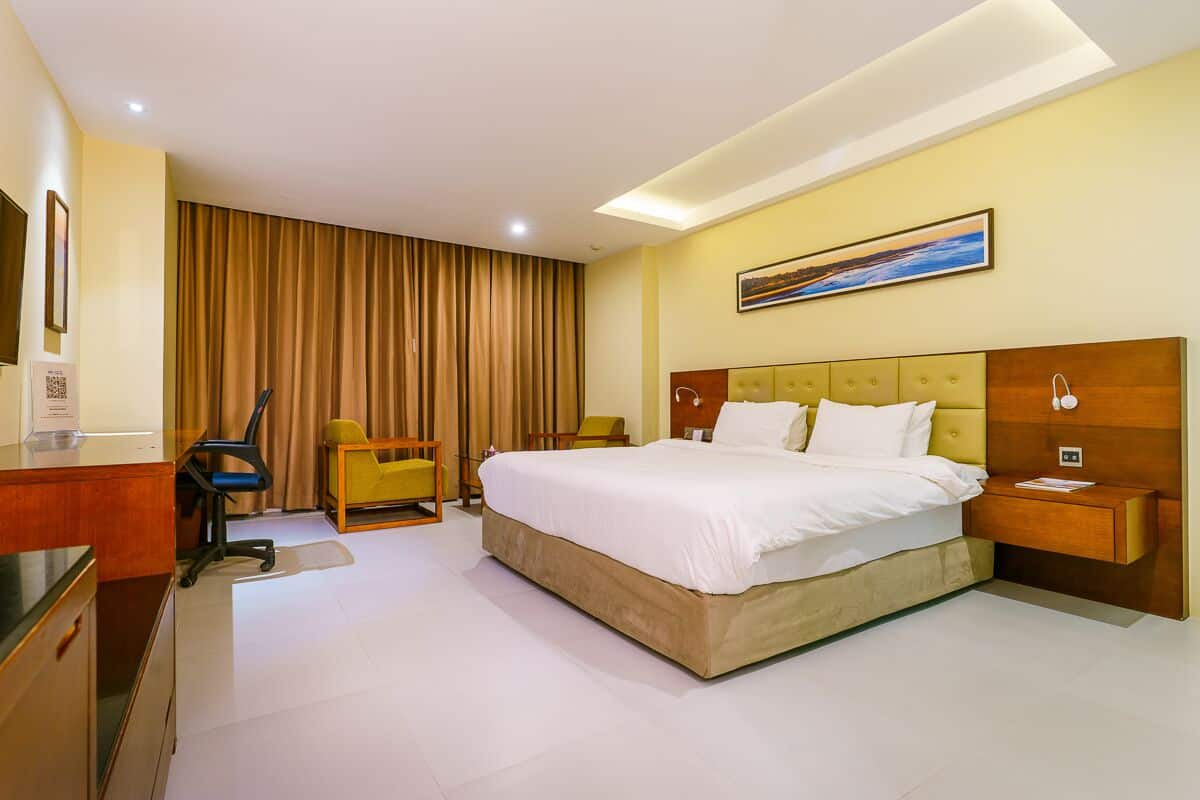A hotel room with a large bed, a desk, a chair, a nightstand, and a painting on the wall.