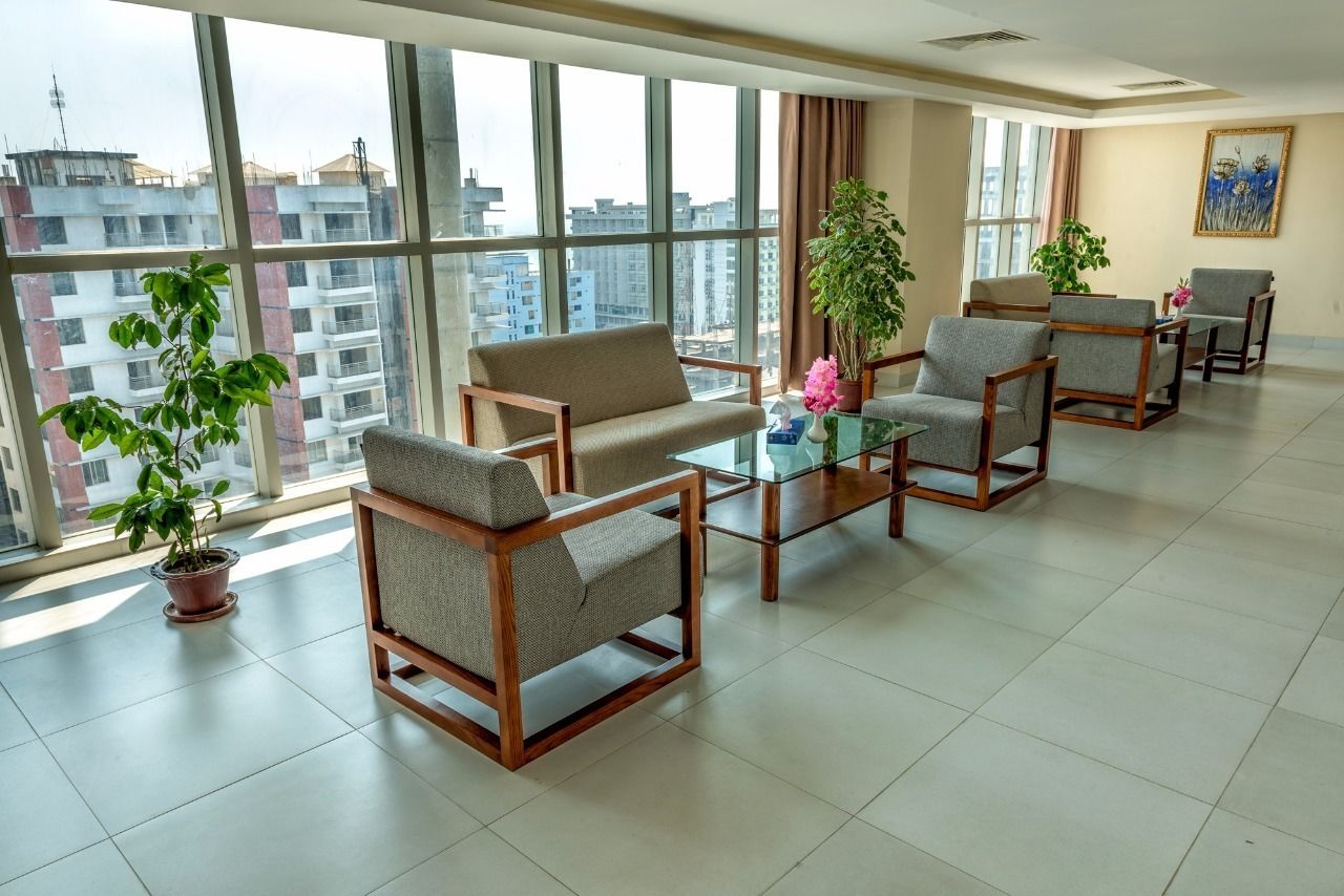 A spacious lobby with large windows, a sofa, armchairs, a coffee table, and potted plants.