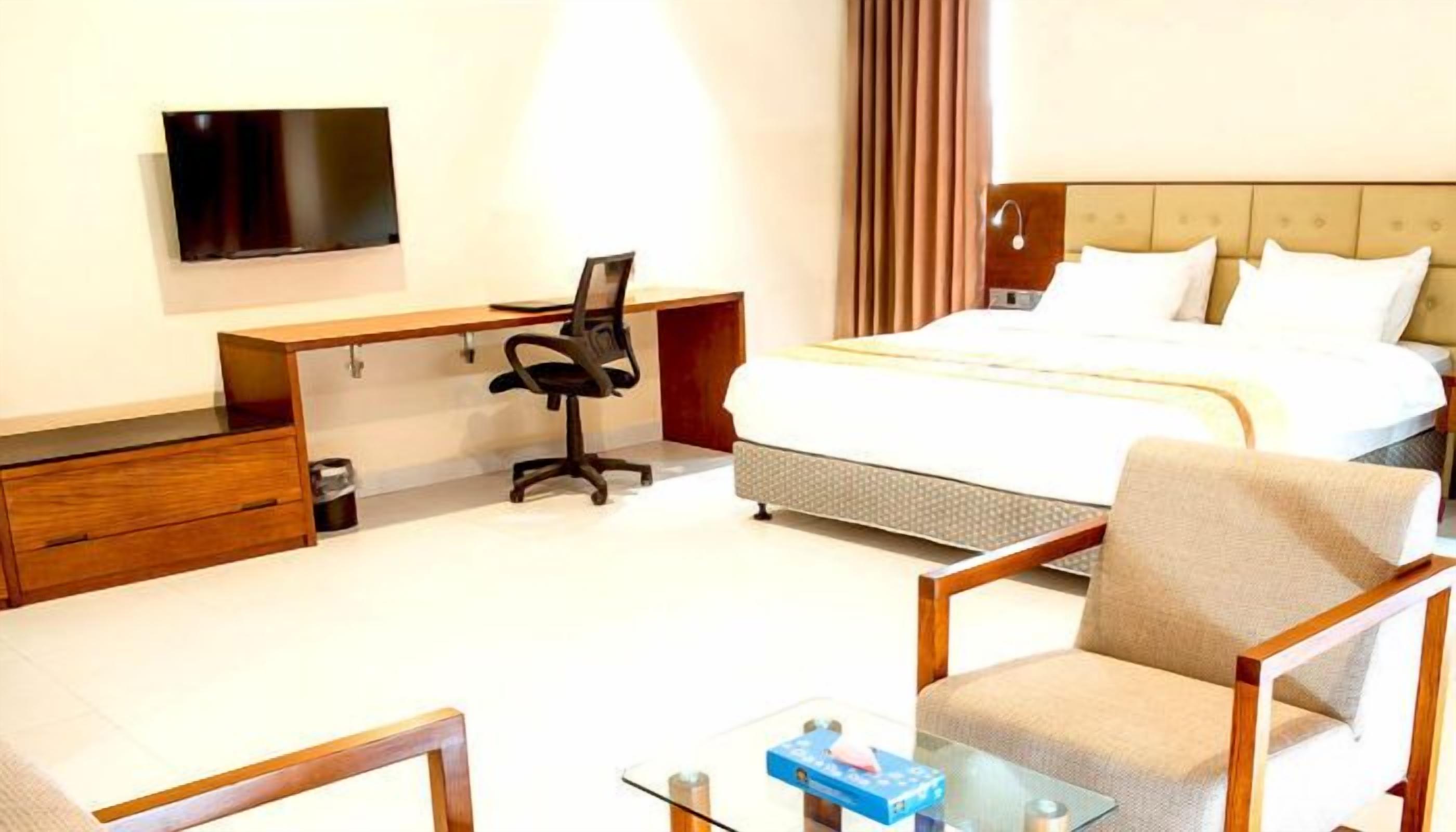 A hotel room with a bed, a desk, a chair, a TV, and a bedside table.