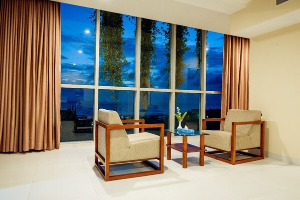 A room with two wooden-framed chairs and a small table, large windows with curtains, and a view of trees and sky. - Best Western Heritage (Cox's Bazar)