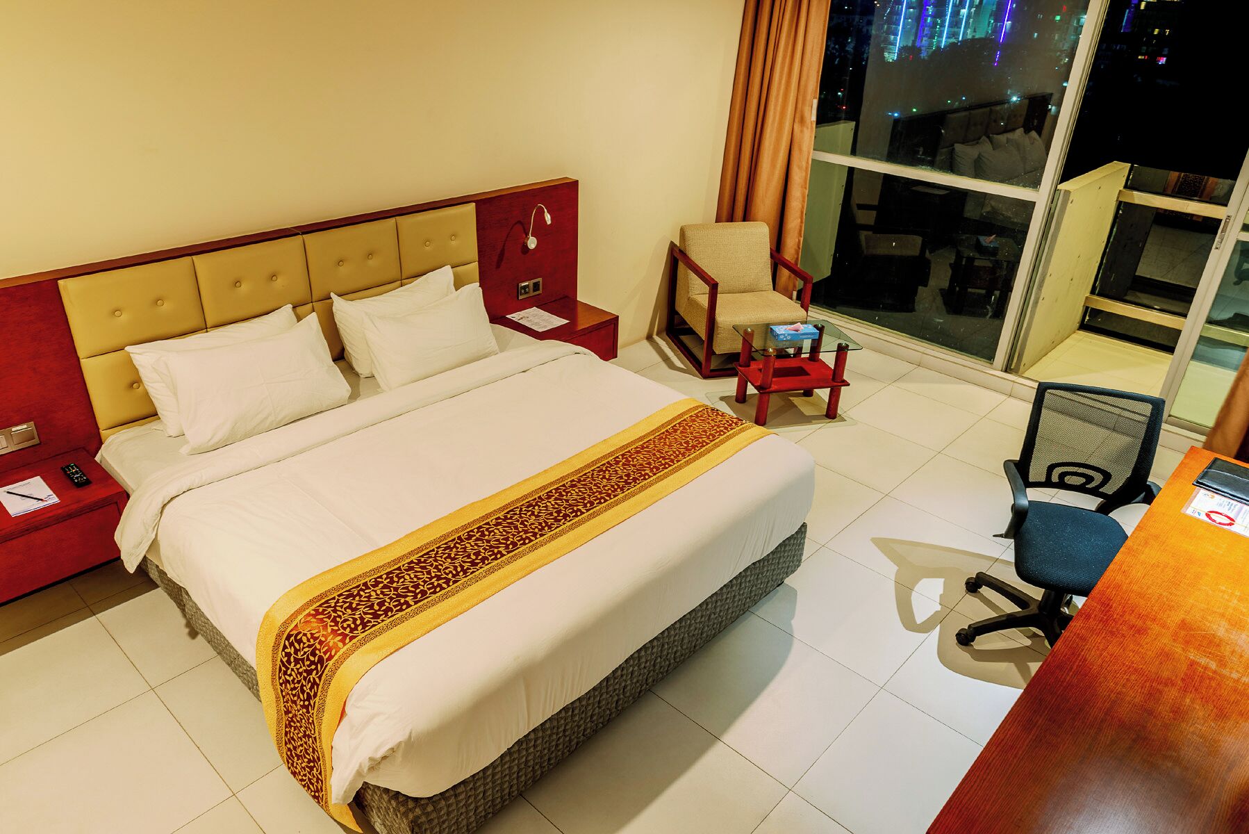 Une chambre d’hôtel avec un lit, une chaise, un bureau et une grande fenêtre donnant sur la ville.