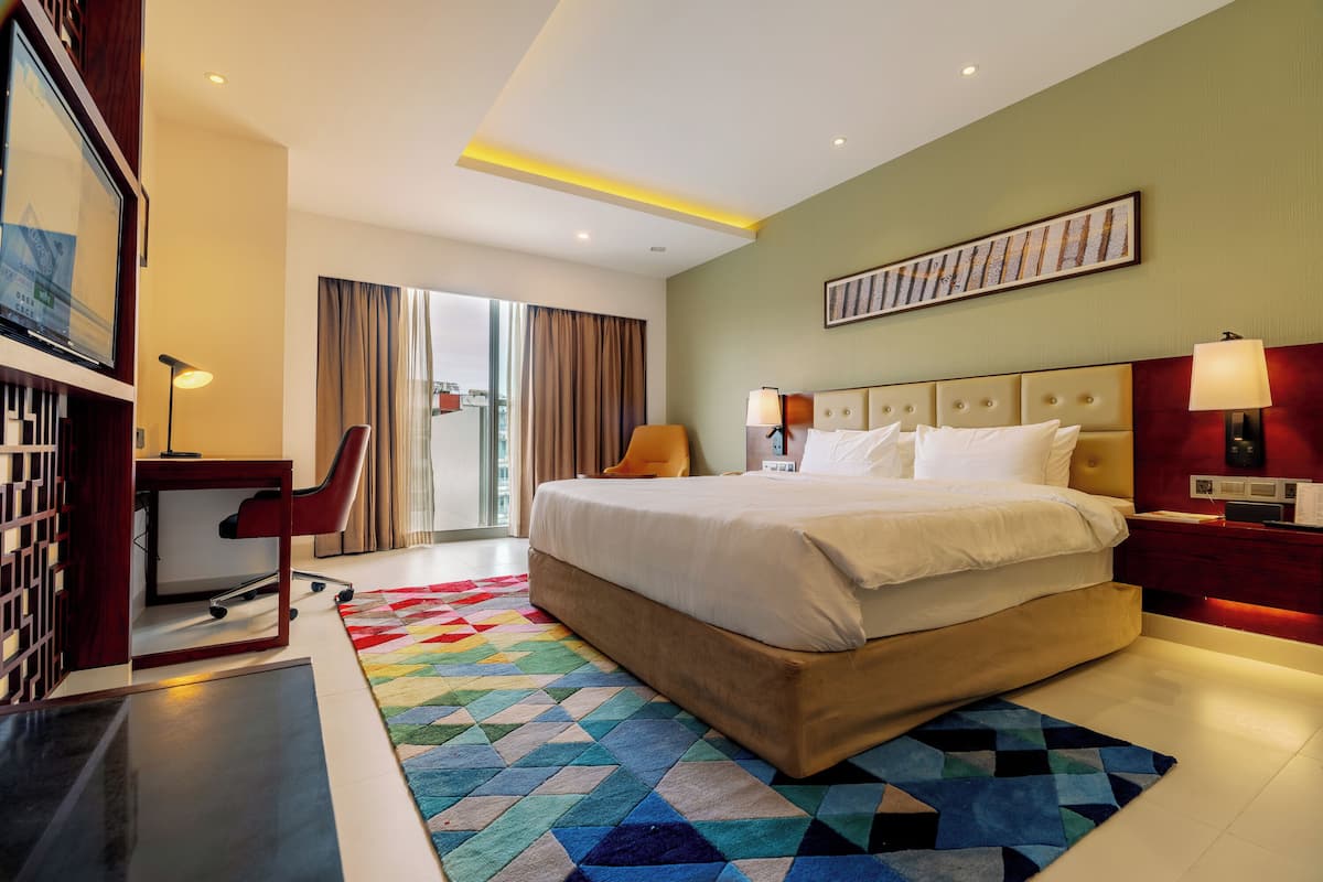 A hotel room with a bed, desk, chair, and a colorful rug.