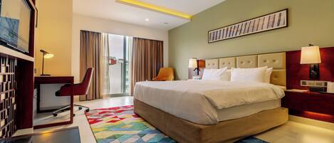 A hotel room with a bed, desk, chair, and a colorful rug.
