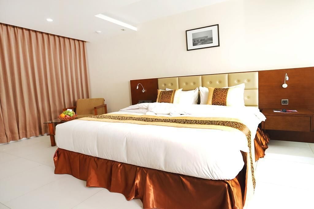 A hotel room with a large bed, a nightstand, a chair, and a window with curtains.