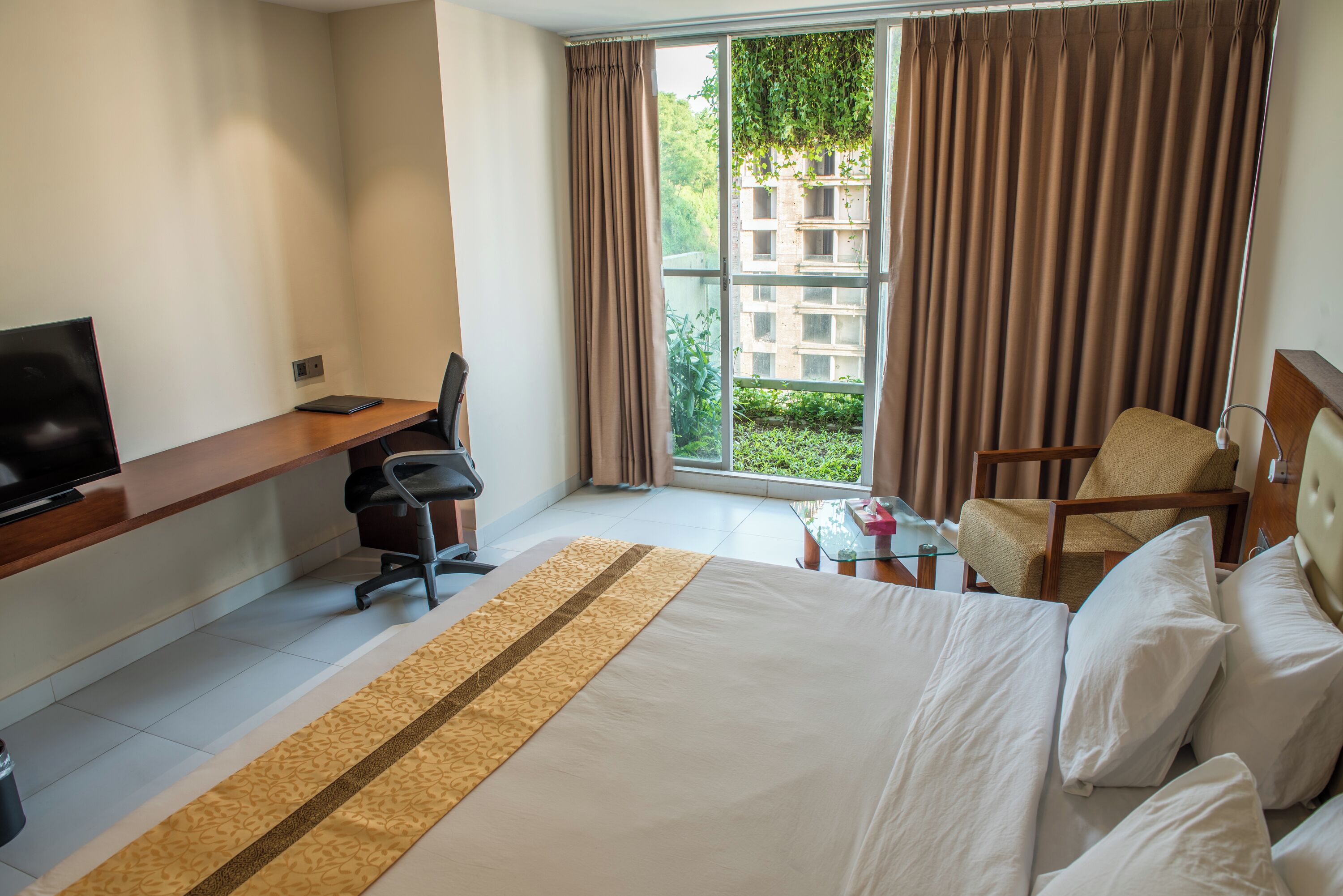 A hotel room with a bed, a desk with a chair, a television, and a window with curtains.