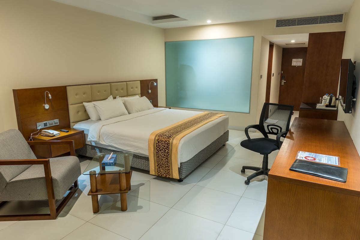 A hotel room with a bed, a desk, a chair, a small table, and a TV.