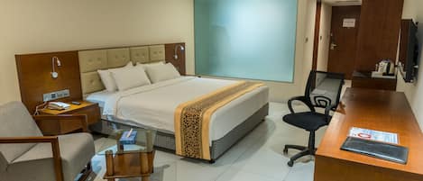 A hotel room with a bed, a desk, a chair, a small table, and a TV.
