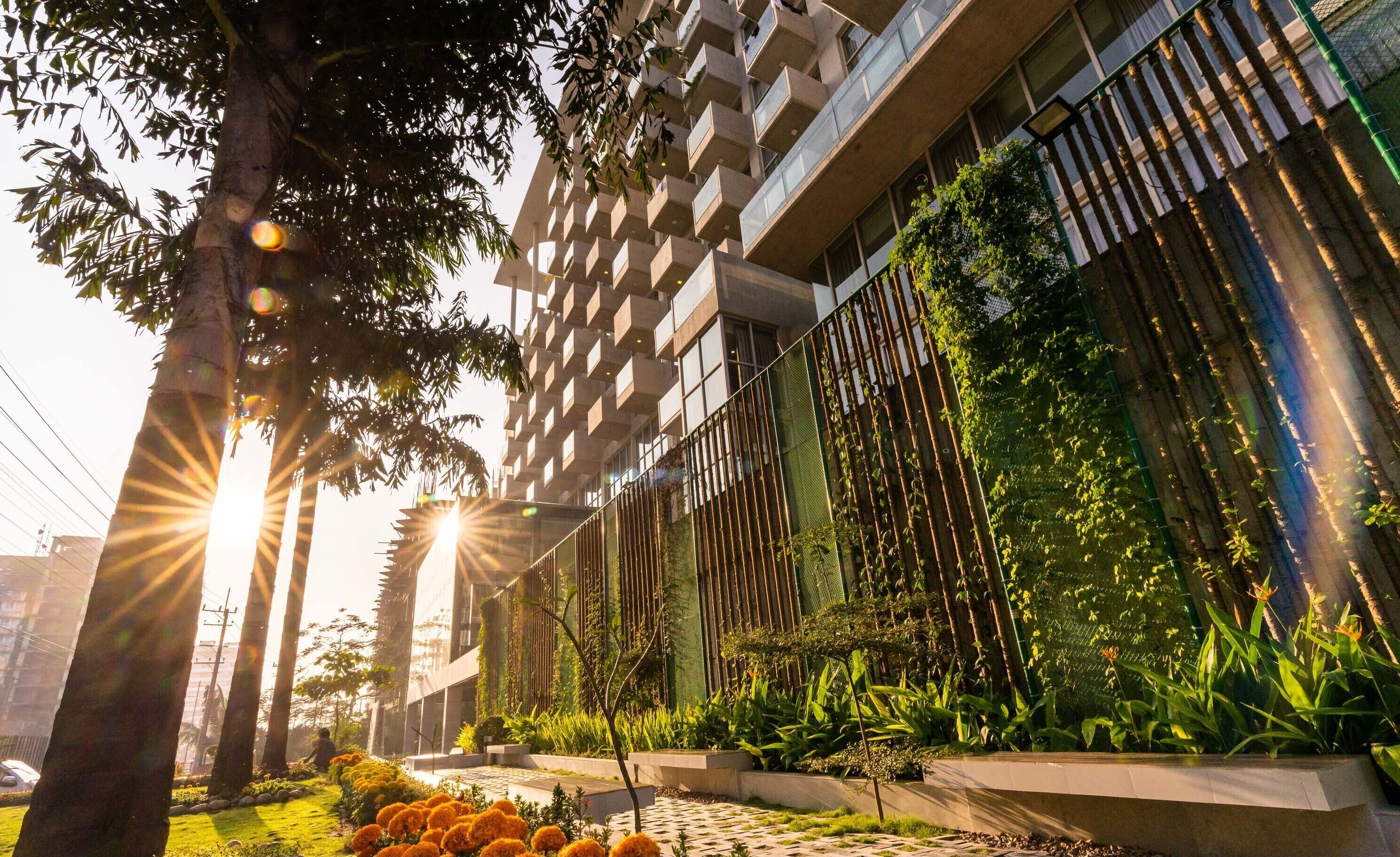 A modern building with a unique facade, a well-maintained garden with various plants, and a clear sky.