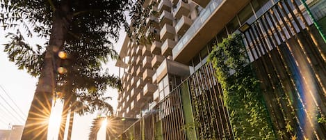 A modern building with a unique facade, a well-maintained garden with various plants, and a clear sky.