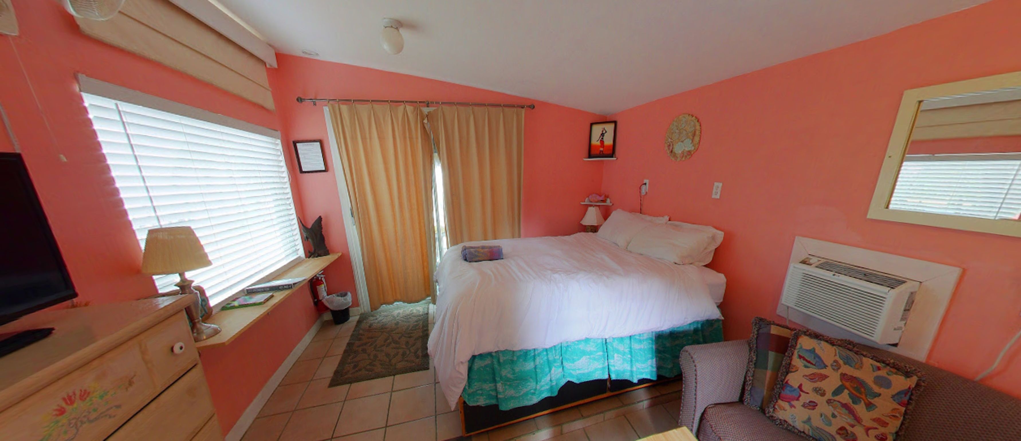 Une chambre à coucher comprenant un lit, une télévision, un bureau et une fenêtre avec des stores.