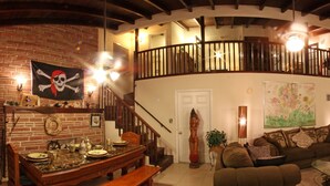 Amplia sala de estar con una mesa de comedor de madera, un sofá y una escalera que conduce a un nivel superior.
