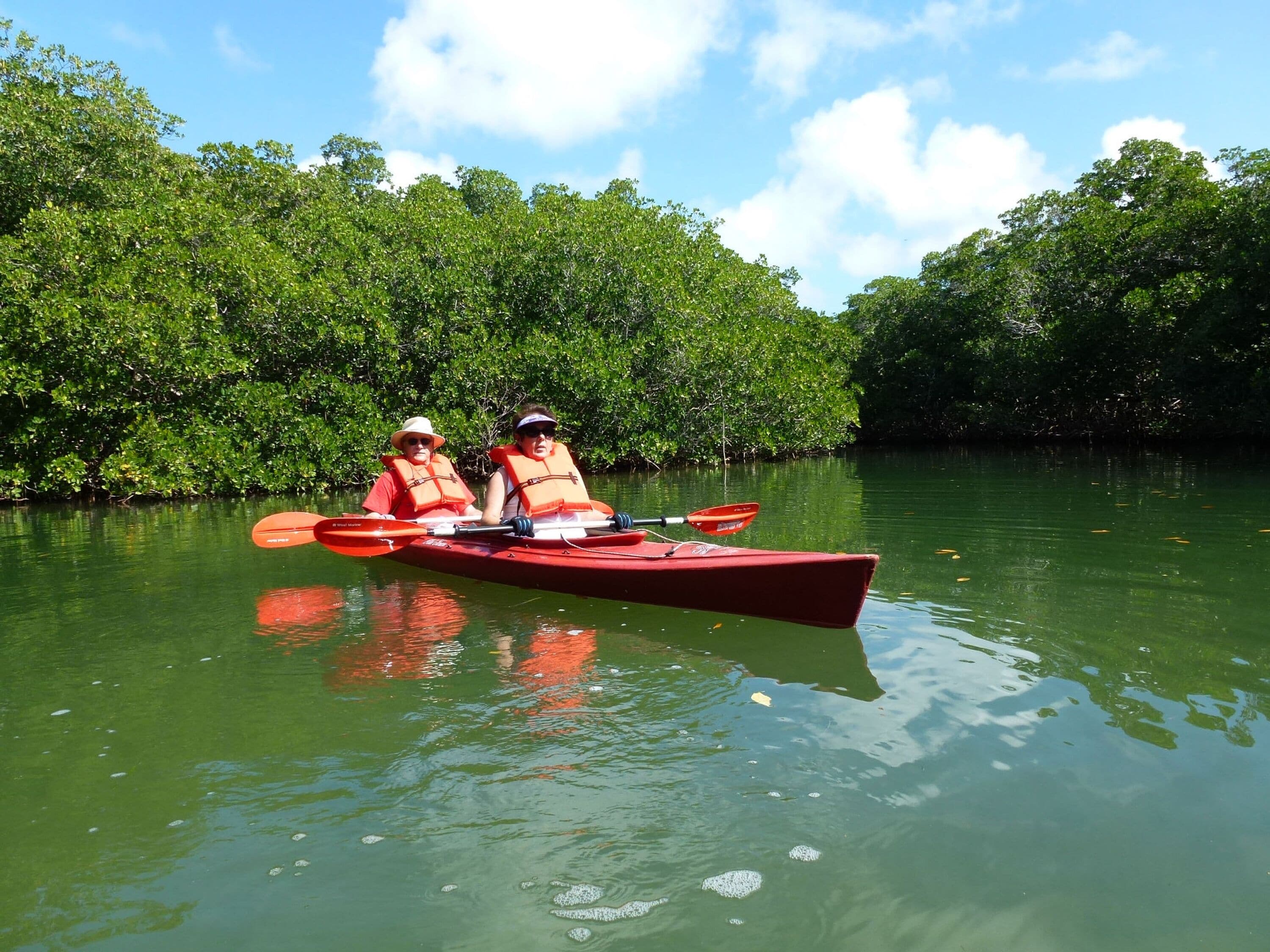 Deux personnes dans un kayak rouge sur une rivière paisible, entourée d’une végétation luxuriante.