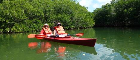 Deux personnes dans un kayak rouge sur une rivière paisible, entourée d’une végétation luxuriante.