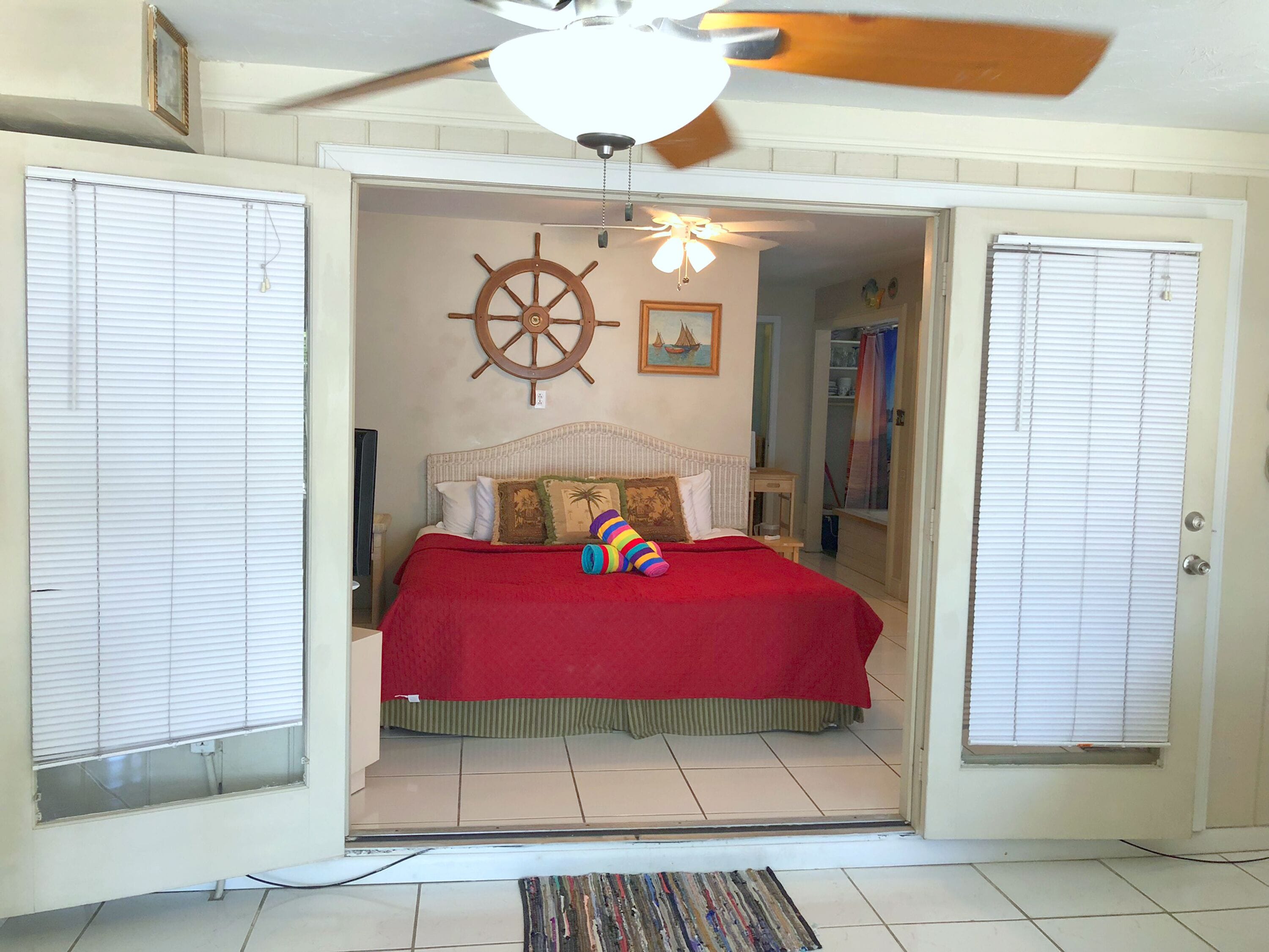 Een slaapkamer met een bed, een plafondventilator, een decoratie van een scheepsschroef en een deur naar een andere kamer.