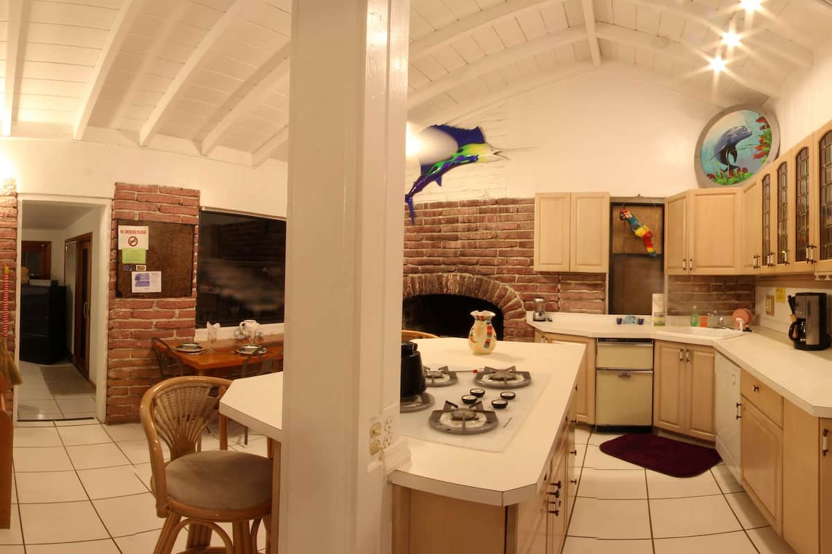 A kitchen with a brick wall, wooden cabinets, a gas stove, and a dining area with wicker chairs.