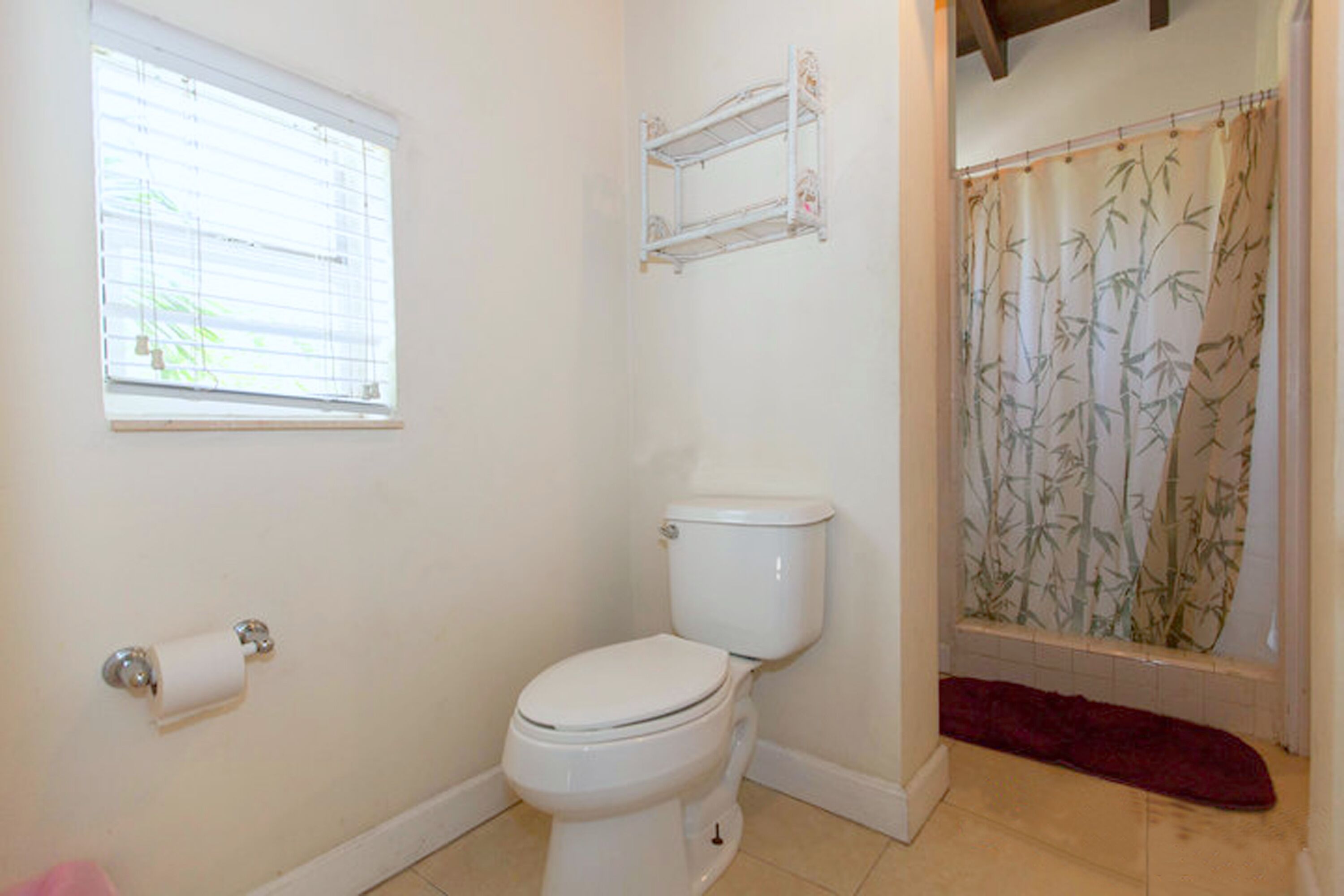 Une petite salle de bain avec des toilettes, une fenêtre avec des stores et un rideau de douche orné d’un motif en bambou.