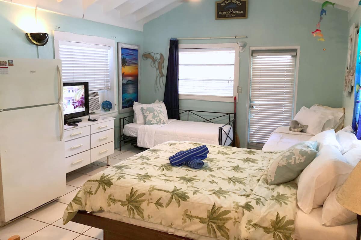 A bedroom with two beds, a TV, a refrigerator, and a painting on the wall.