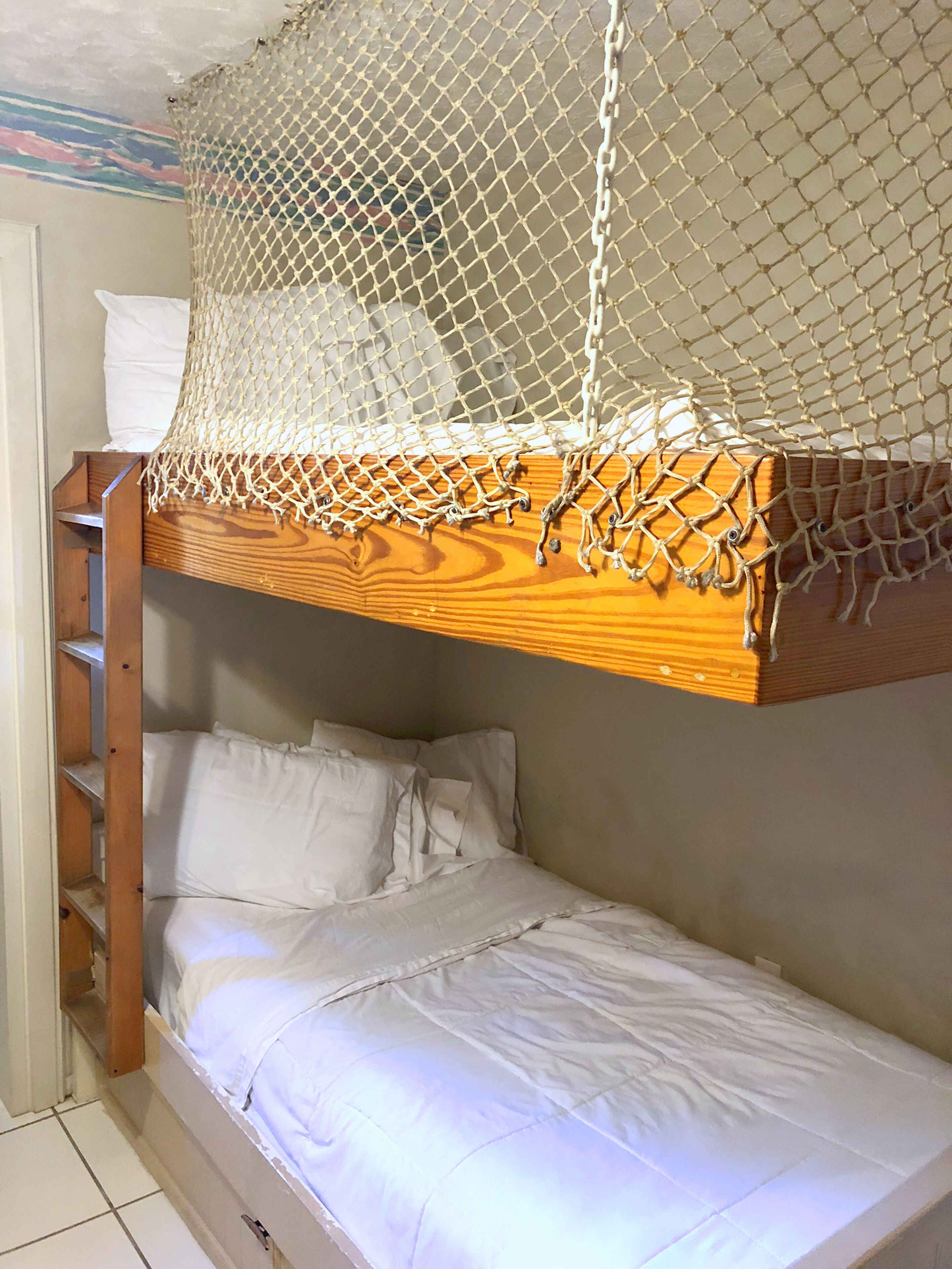 A bunk bed with a net canopy, wooden headboard, and white bedding.