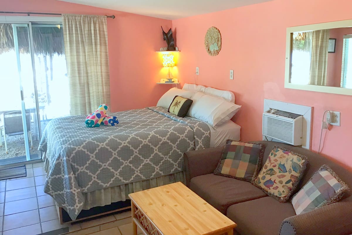 A bedroom with a bed, a nightstand, a lamp, a sofa, and a window with curtains.